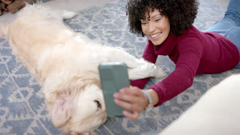 Happy-biracial-woman-taking-photo-with-golden-retriever-dog-using-smartphone-at-home,-slow-motion