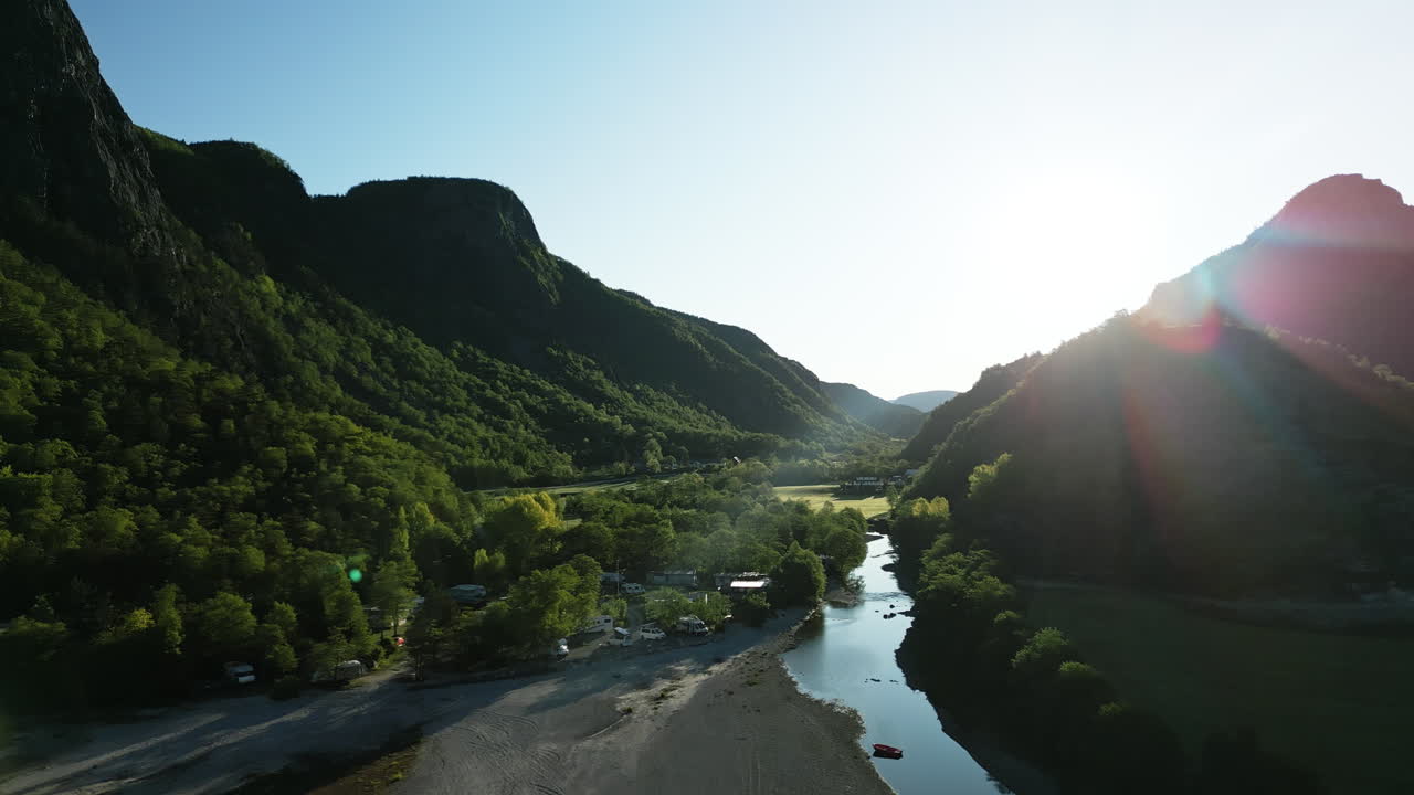 Morning drone shot of the Norwegian landscape at Lake Tysdalsvatnet with a campsite by the lake in the foreground. The Norwegian mountain landscape is illuminated by the sun