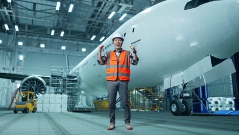 cuerpo lleno de ingeniero masculino asiático con casco de seguridad de pie y gritando meta celebrando trabajando con aviones en el hangar