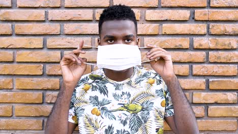 Afro-Mann-Zeigt-Schritt-Für-Schritt,-Wie-Man-Eine-Maske-Aufsetzt,-Um-Eine-Kontamination-Mit-Dem-Coronavirus-Sars-Cov-2-Zu-Vermeiden