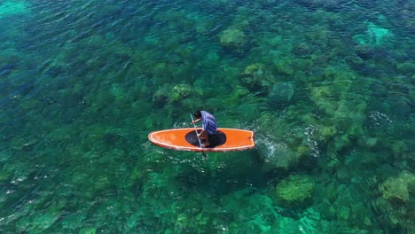 turista masculino remando en una tabla de paddle naranja en el agua clara del parque marino tagbak