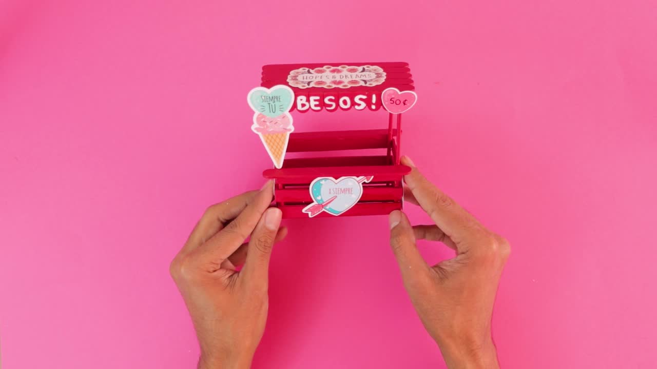 Putting heart sticker on handmade miniature Valentine's kissing booth.