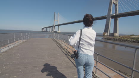 follow shot of a young woman walking down the pier and enjoying the amazing view of the river with a bridge. low tide.tagus river. contemplation in solitude. architectural wonder