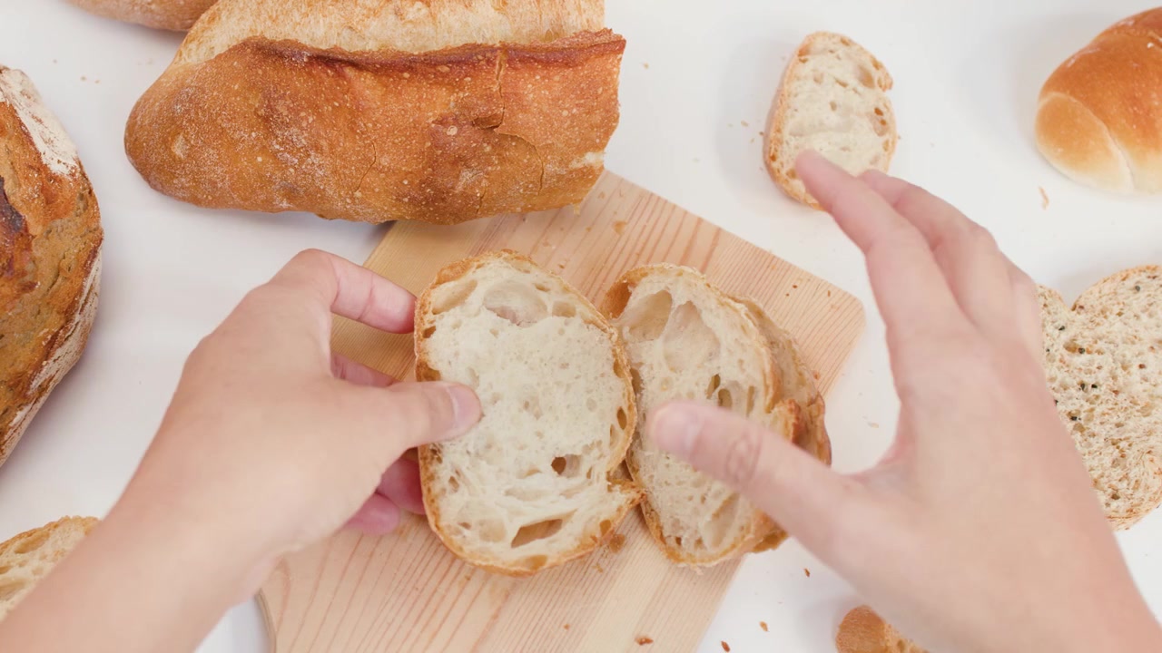 Top-down view of hands organizing fresh crusty bread slices on a wooden cutting board.