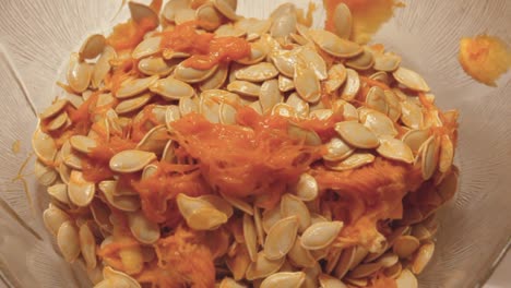 Top-down-view-of-an-adult-hand-wearing-glove-scooping-out-pumpkin-guts-and-seeds-into-a-bowl