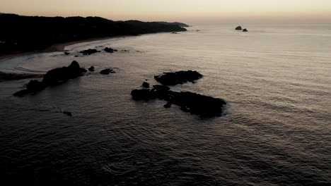 aerial tilt up shot of peaceful coastline of punta cometa coastline with rocks in oaxaca,mexico - beautiful evening with yellow sunset in backdrop