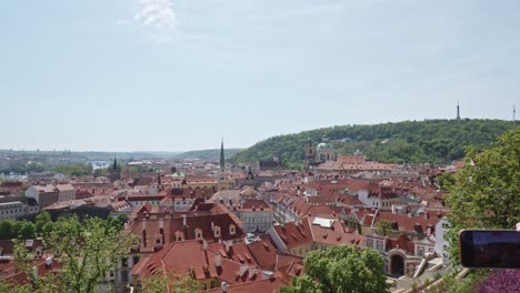 hand-taking-photo-with-a-phone-of-breathtaking-panorama-of-Prague's-Old-Town-with-red-rooftops-in-Czech-Republic