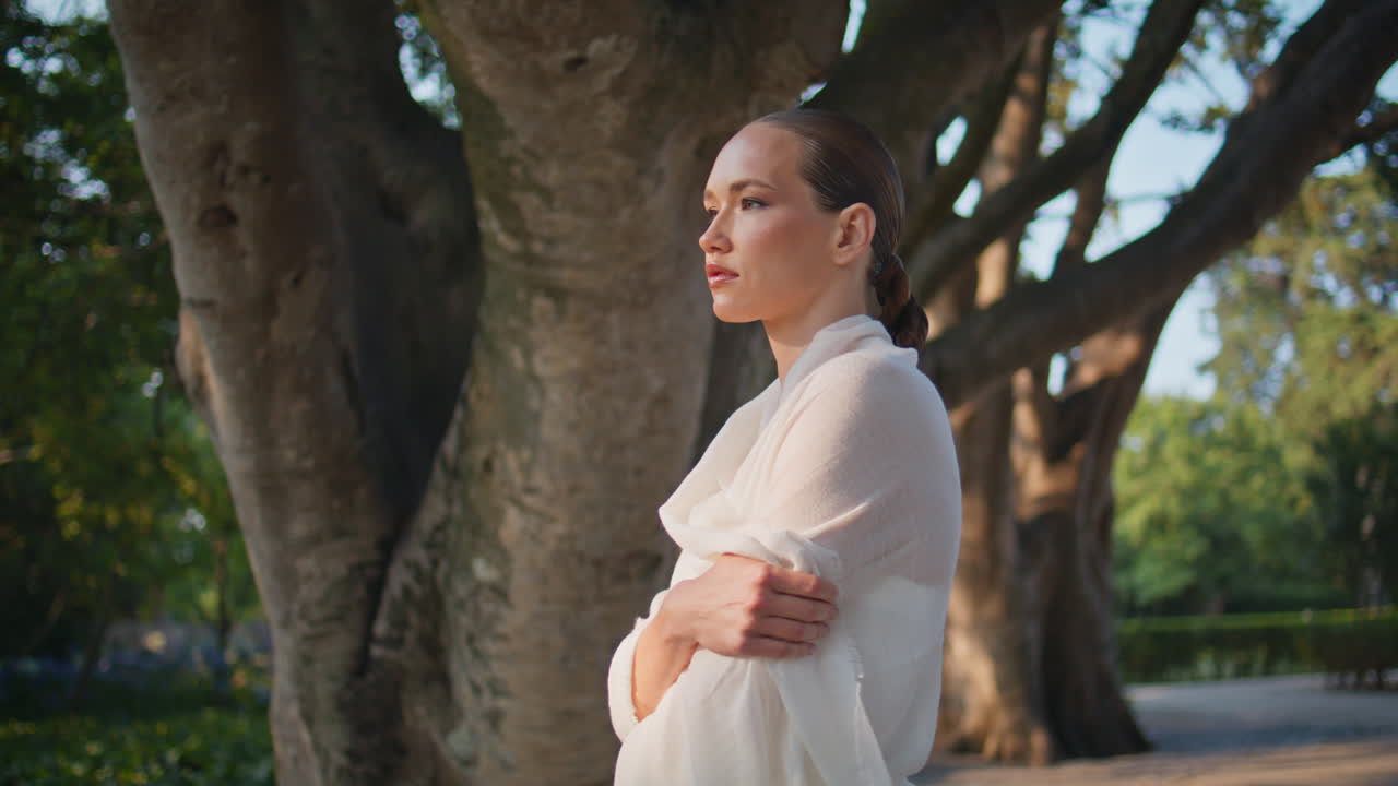 부드러운 소녀는 나무에 서서 멀리서 가까이서 쳐다보고 있다.  천을 감싸고 있는 여자