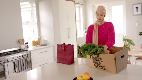 Mujer-Birracial-En-Hijab-Con-Compras-En-La-Cocina-De-Casa-Con-Espacio-Para-Copiar,-Cámara-Lenta