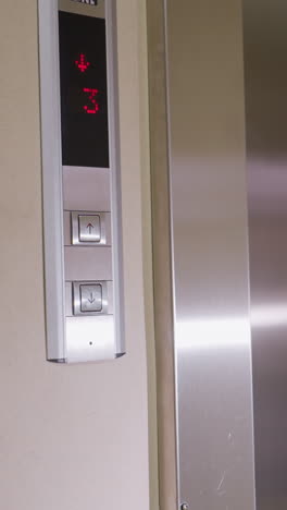 elevator control panel with up and down arrows, digital display showing floor 3 in red, modern metallic finish with sleek design. display indicates elevator movement in office building or high-rise