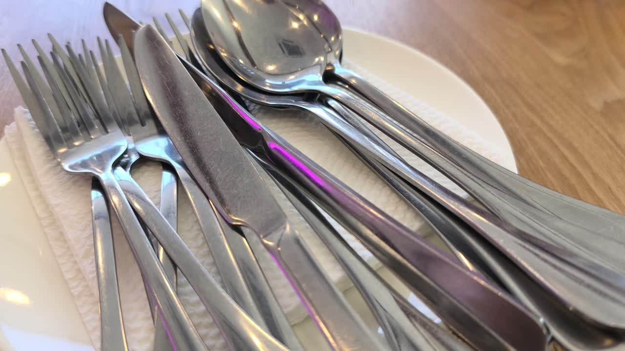 Clean silverware rests neatly on a white plate and napkin. The cutlery is set on a dining table. Everything is ready for the upcoming meal service