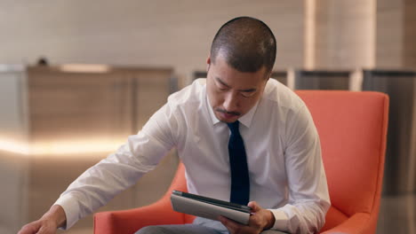 Japanese-Businessman-using-digital-tablet-technology-in-hotel-lobby