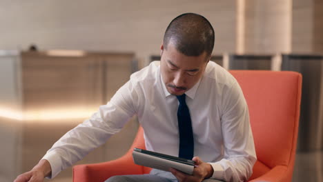 hombre de negocios japonés usando tecnología de tableta digital en el vestíbulo del hotel