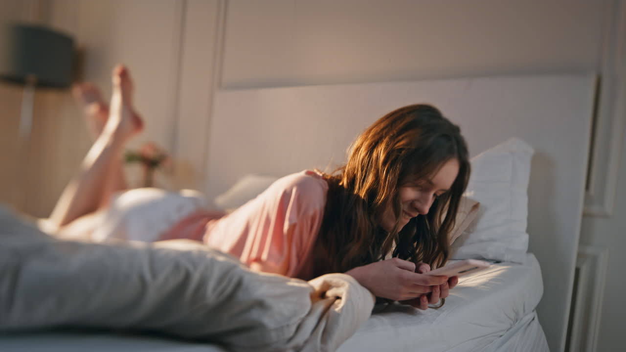 Smiling girl playing mobile phone games online at home. Relaxed teenager typing