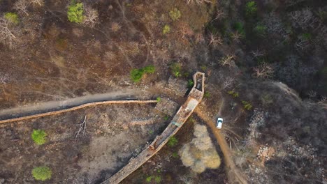 Toma-De-Arriba-Hacia-Abajo-De-Un-Antiguo-Muro-De-Fuerte-Con-Un-Auto-Blanco-Estacionado-Al-Lado-En-Un-Denso-Bosque-De-La-India-Central