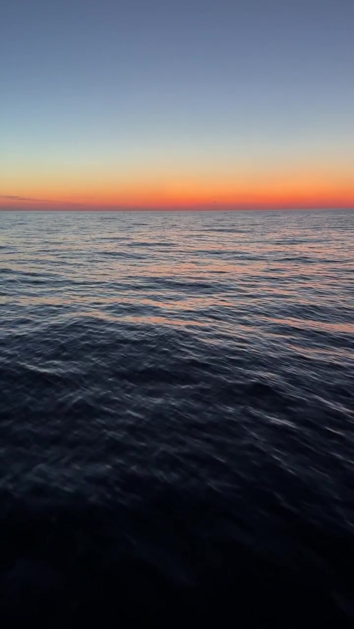 A Calm Sea Stretches to the Horizon Under a Vivid Sunset Sky - Vertical Shot