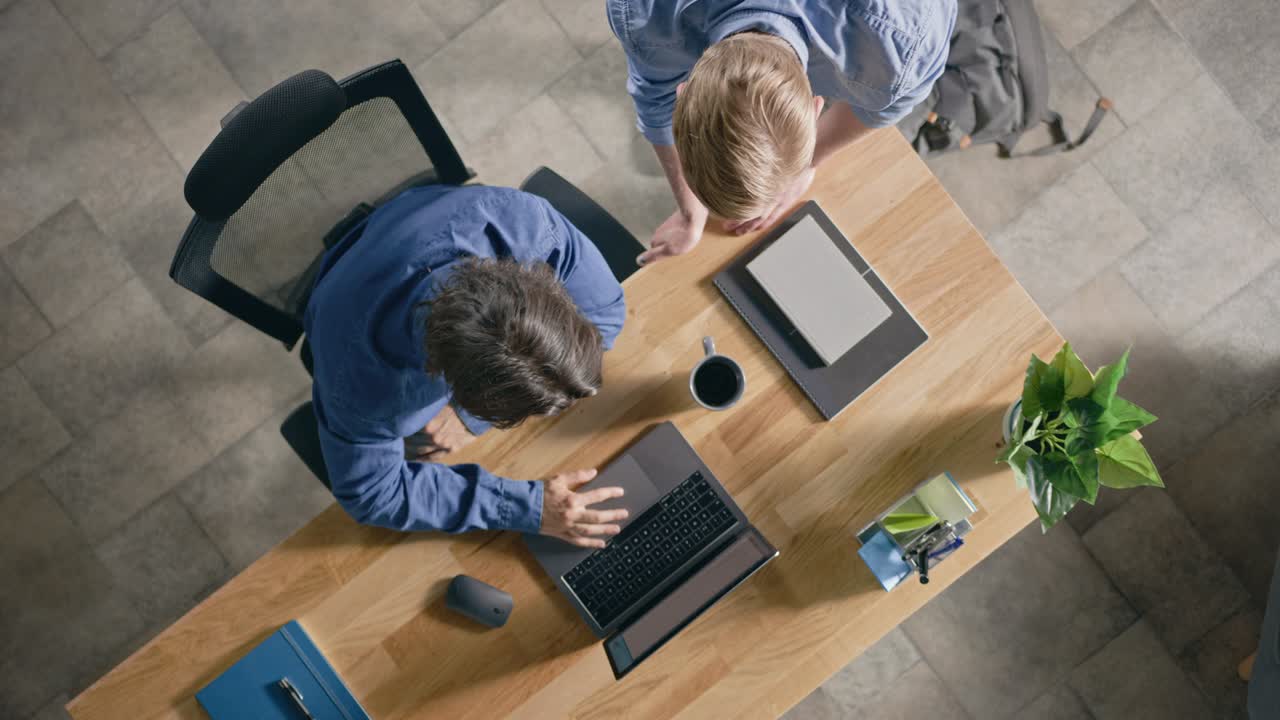 Topbillede: Forretningsmand arbejder ved sit skrivebord på en bærbar computer, taler med sin chef og lytter til råd om projektkonceptet. To mænd diskuterer arbejde