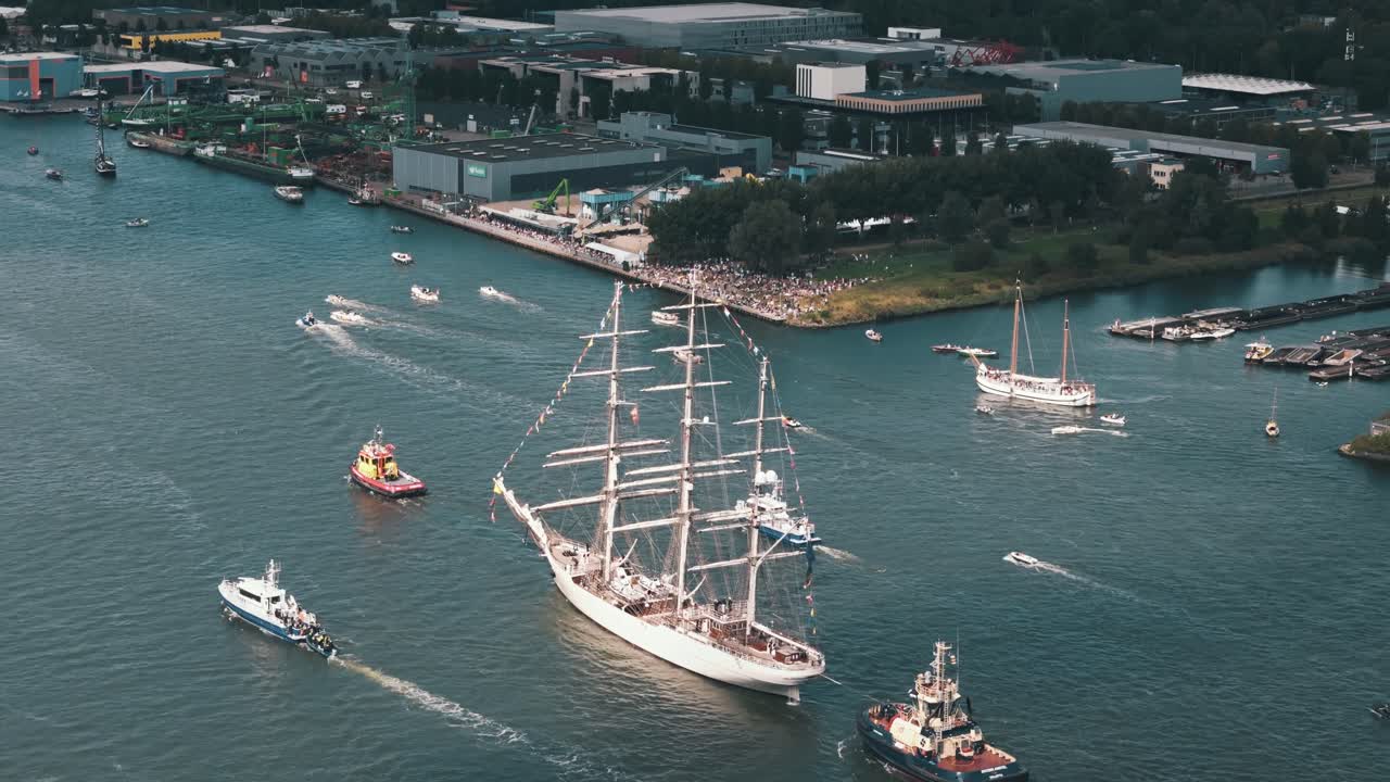A tugboat pulls a white-sailed ship through the Amsterdam sail-out