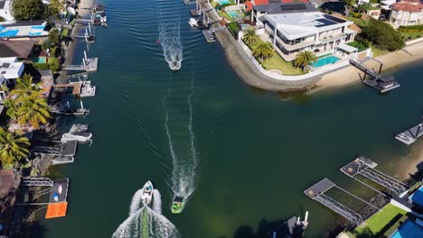 drone footage captures a speedboat moving through a residential canal lined with luxury homes under bright daylight, with smooth camera movement and clear reflections