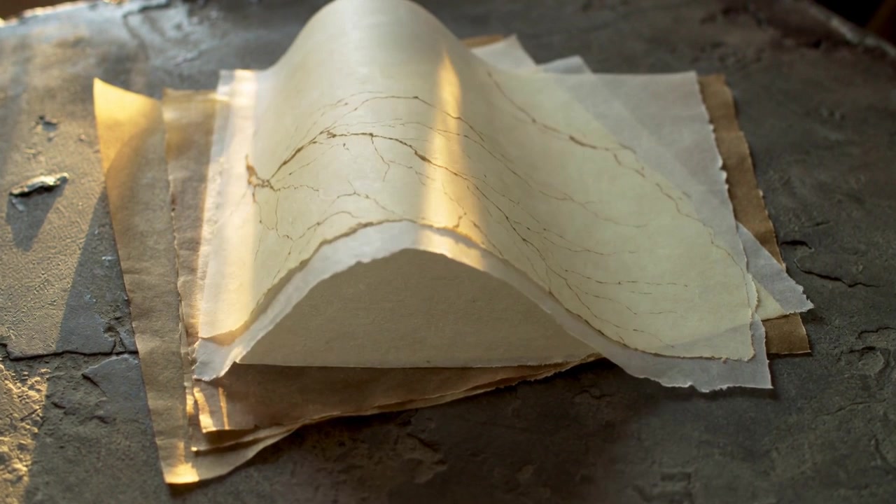 Lifting top handmade deckled paper sheet curling, folding on workshop workbench under warm sunlight