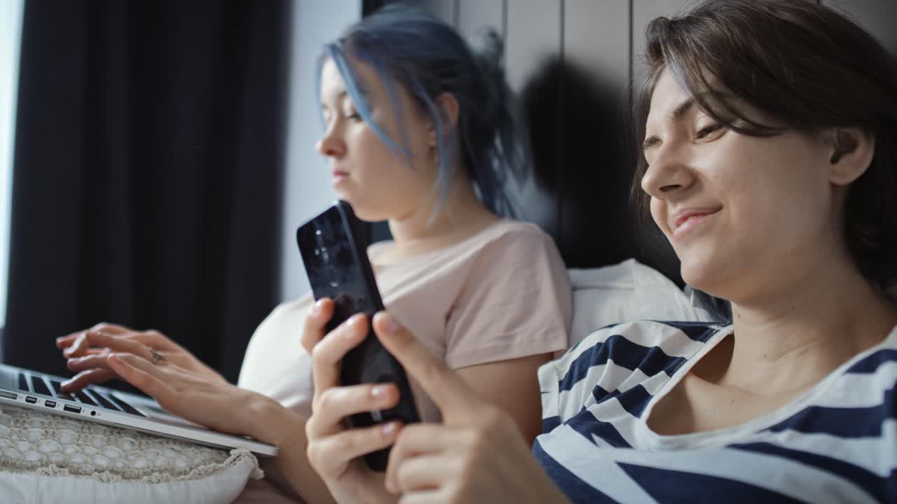 video de una pareja de lesbianas en la cama con portátil y teléfono