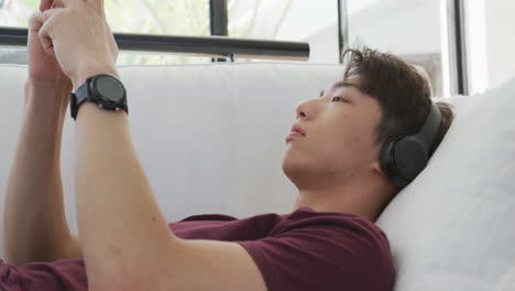 asian male teenager wearing headphones and using smartphone in living room