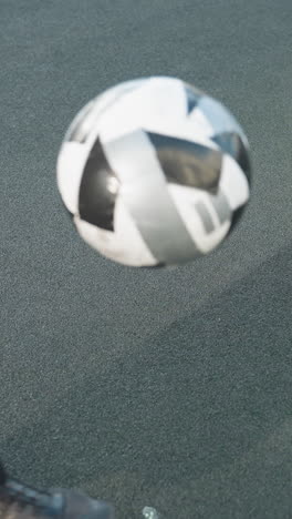 el futbolista con capucha patea hábilmente la pelota de fútbol hacia arriba en el campo deportivo urbano, capturando el movimiento dinámico y el enfoque intenso. el fondo incluye edificios residenciales y postes de portería