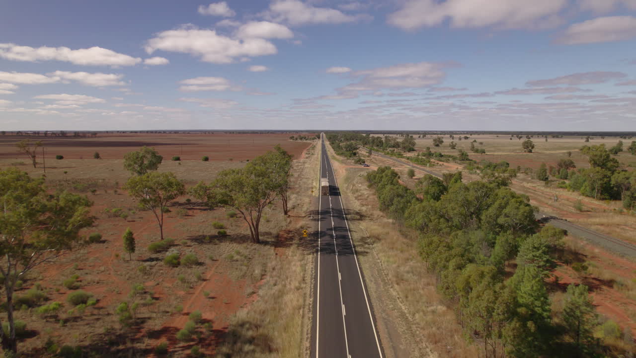 We follow a long haul truck as it makes its way along a highway in the red Australian outback.