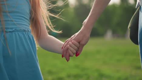 lower view of mother and daughter holding hands swaying while walking together on green grass in park summer afternoon, gentle motion showing bond and affection, warm light, family connection
