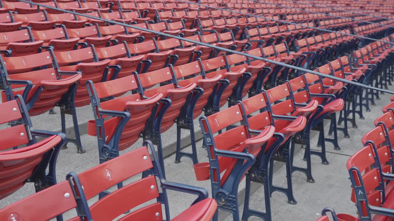 Rows of empty red stadium seats with navy blue metal frames arranged in sections at a baseball park or sports venue