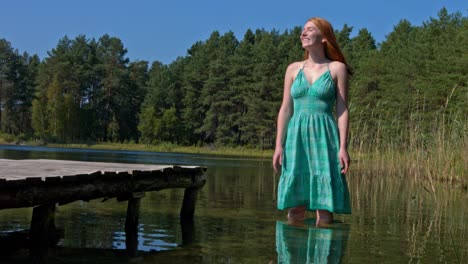 mujer pelirroja feliz parada en el lago y salpicando agua cayendo junto a ella