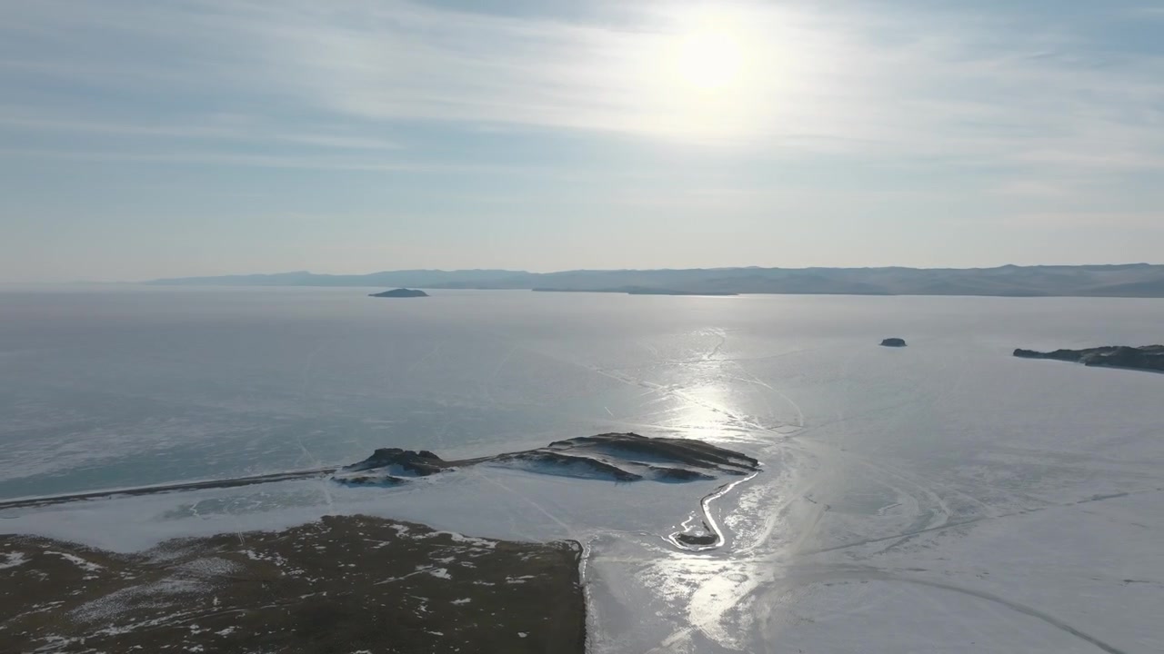 Riprese con drone del Lago Baikal ghiacciato con costa gelata, piccole isole e riflesso del sole sul ghiaccio, paesaggio invernale in Siberia, Russia, con vasti spazi aperti.
