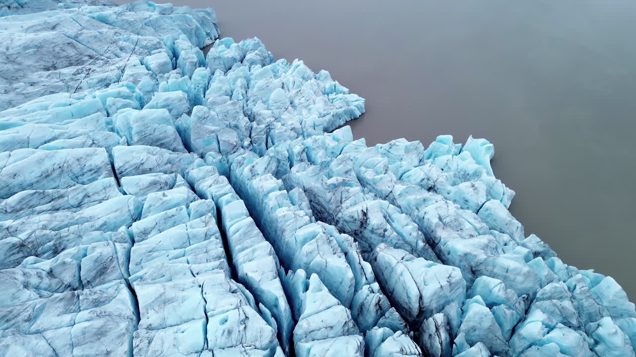 Vista aerea con drone delle formazioni di ghiaccio del ghiacciaio Breiðamerkurjökull vicino alla laguna di Jökulsárlón, Islanda. Blocchi di ghiaccio blu intenso e profonde crepe formano disegni astratti e congelati nel paesaggio glaciale