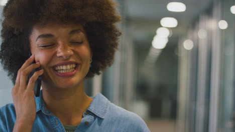 Smiling-Businesswoman-Standing-In-Corridor-Of-Modern-Office-Talking-On-Mobile-Phone