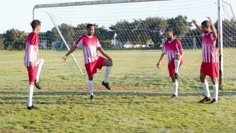 soccer players warming up on field, stretching in front of goal net