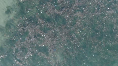 alta altitud de arriba hacia abajo disparo de dron de agua contaminada llena de basura flotando sobre arrecife de coral muerto en las aguas tropicales turquesa de bali indonesia