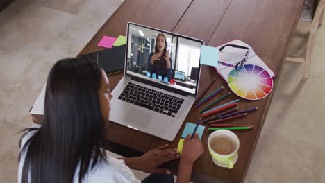 Eine-Afroamerikanische-Frau-Macht-Sich-Notizen,-Während-Sie-Zu-Hause-Einen-Videoanruf-Mit-Einer-Kollegin-Auf-Dem-Laptop-Führt