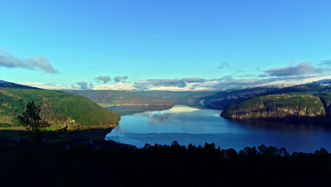 a reveal shot of a calm lake surrounded by mountains with forests in norway