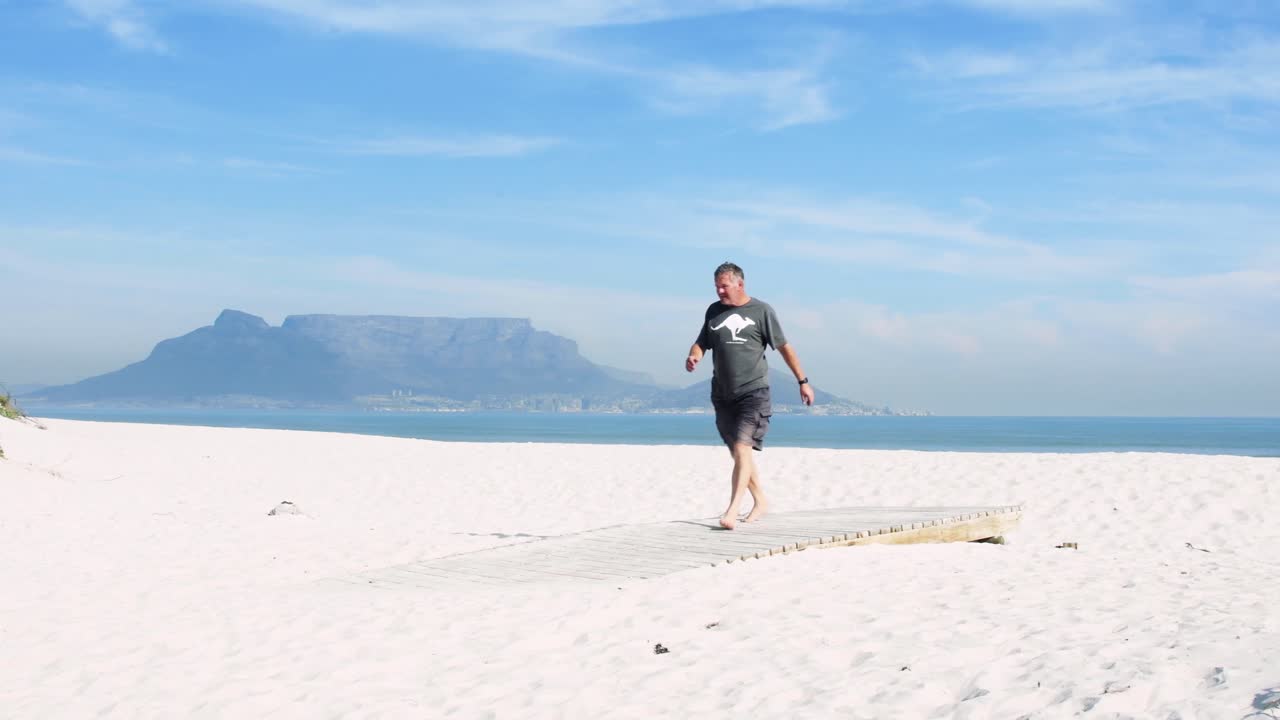 An international tourist walks off Table Bay beach towards a boardwalk with world famous Table Mountain in the background.