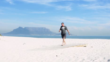 an international tourist walks off table bay beach towards a boardwalk with world famous table mountain in the background.