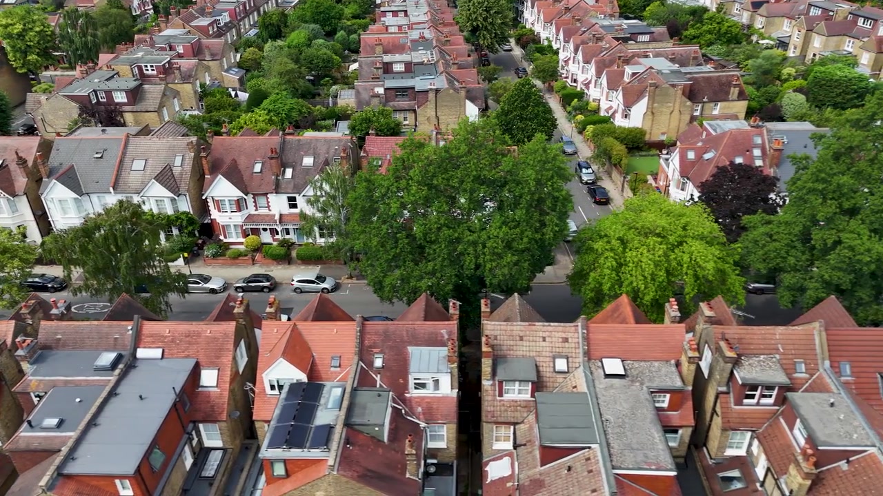 Rijen Edwardiaanse twee-onder-een-kapwoningen met rode pannendaken, erkers en lange achtertuinen langs een rustige straat in West-Londen