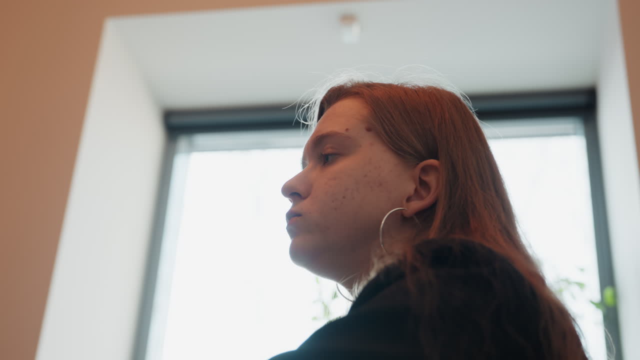 Young caucasian woman eating near window backlit silhouette subtle hand gesture lingering bite and thoughtful expression hoop earrings long hair soft overcast light intimate indoor dining scene