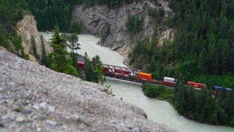 cargo freight train travelling across a river in the beautiful landscape of golden british colombia canada