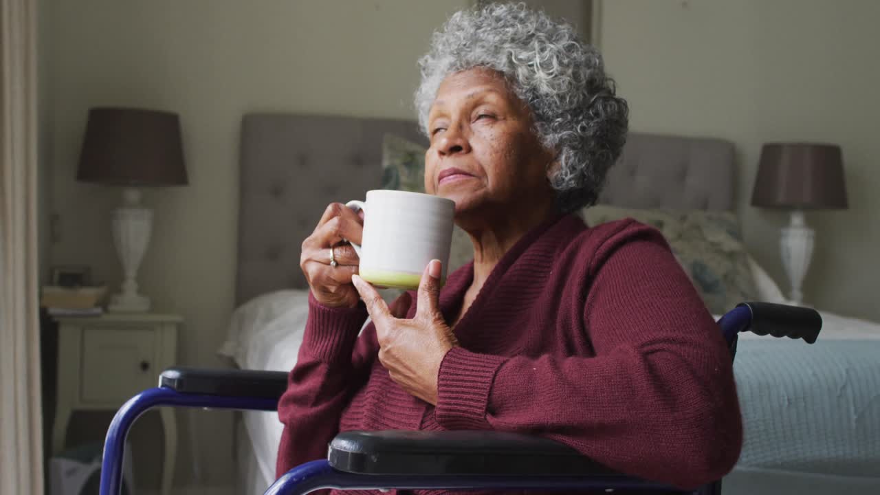 Senior african american woman sitting on the wheelchair drinking coffee at home