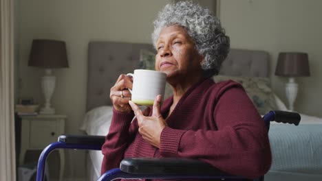 Senior-african-american-woman-sitting-on-the-wheelchair-drinking-coffee-at-home