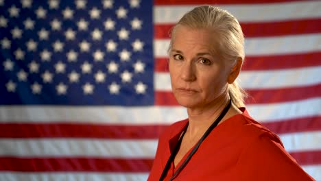 medium tight portrait of the back of blonde nurses head as she turns and looks at camera looking angry and concerned with out of focus us flag