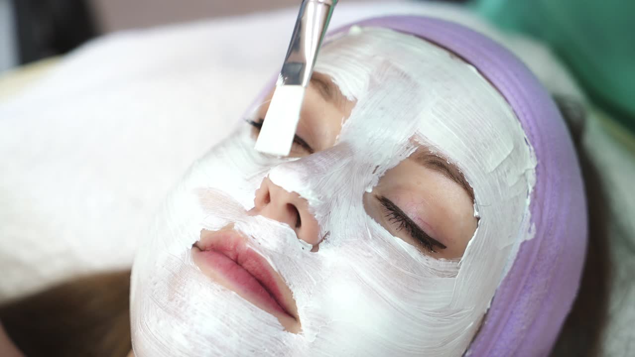 Girl relaxing in spa salon. Beautician applies the mask to the face of beautiful young woman in the spa salon