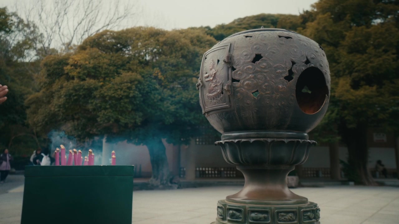 Primo piano di un bruciatore d'incenso sferico in bronzo finemente intagliato che brilla con una fiamma interna, posto su un piedistallo all'interno del complesso del tempio vicino al Grande Buddha di Kotoku-in a Kamakura