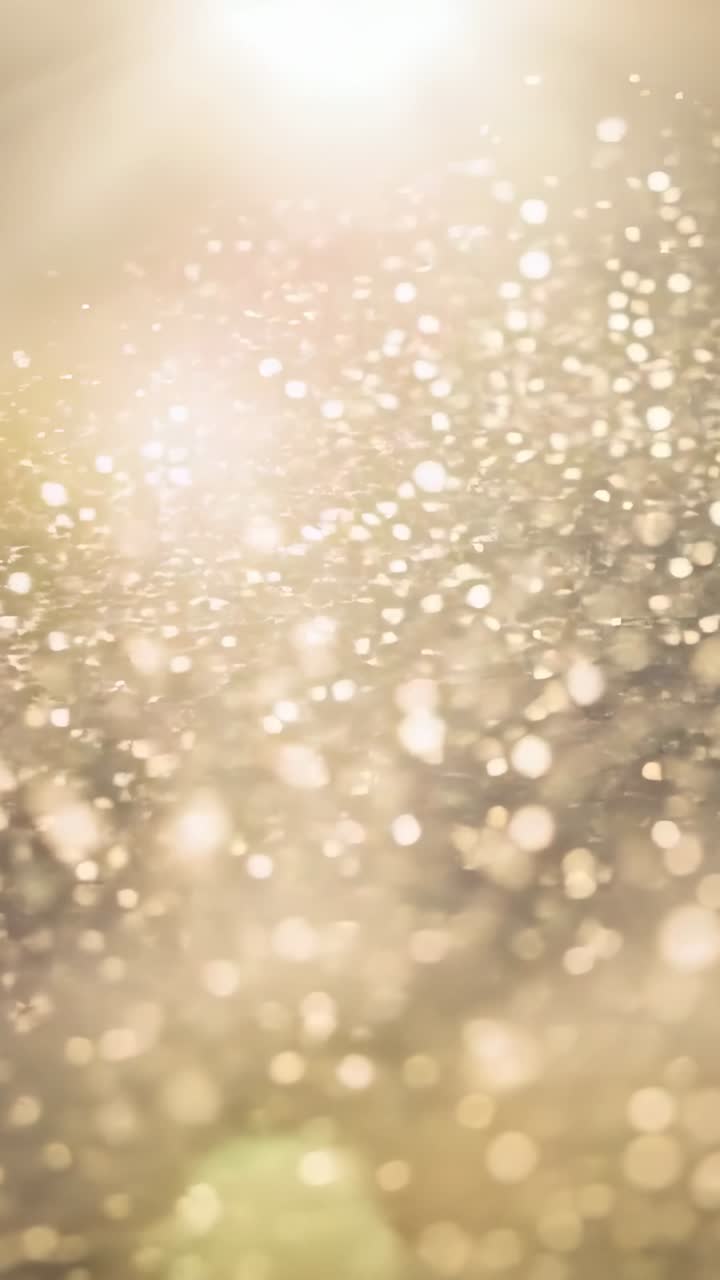 Vertikales Video: Schillernde Nahaufnahme-Bokeh-Partikel, beleuchtet von warmem Licht von oben in der Mitte, bei Fokusverschiebung.
