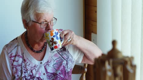 Senior-woman-drinking-coffee-and-looking-through-window-4k